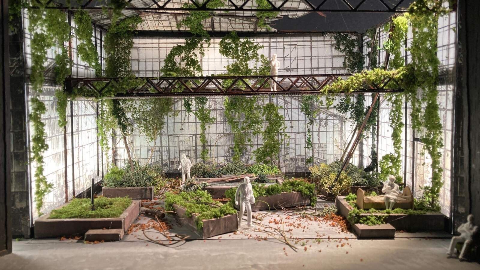 En scenografi modell som visar ett stort växthus. Växthuset är rostigt, igenvuxet och övergivet. Ljus strömmar genom glaset.