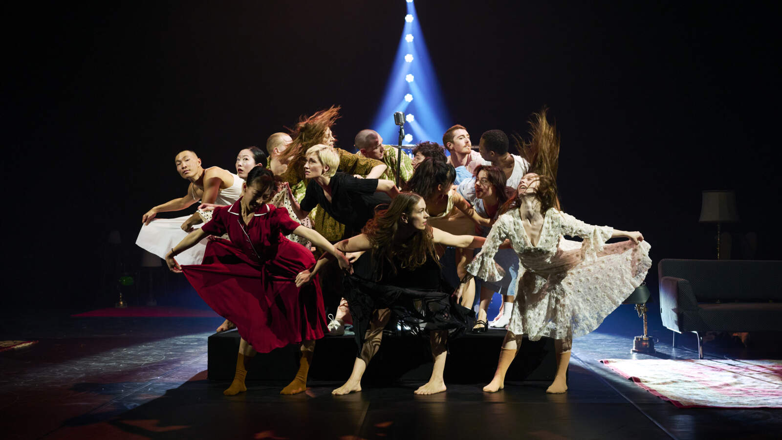 Flera dansare står i en tajt grupp, vissa på golvet, andra uppe på en plattform. Främsta raden sträcker ut deras kjolar.