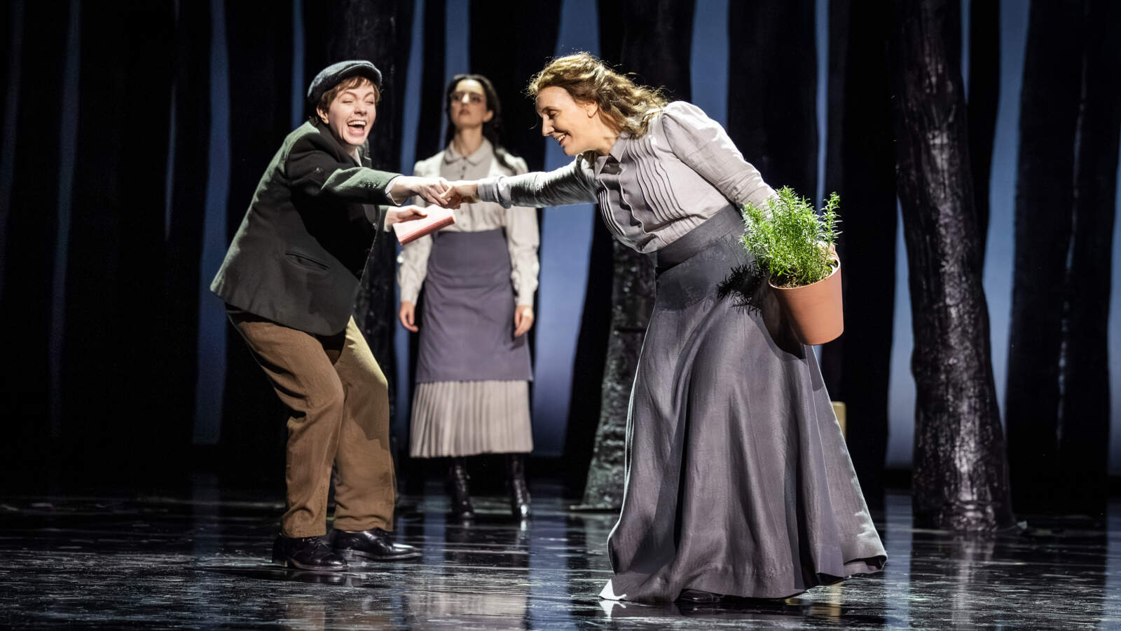 Jenůfa står med en kruka rosmarin i vänstra handen och Janos hand i sin högra. Jano skrattar och drar i Jenůfas hand.