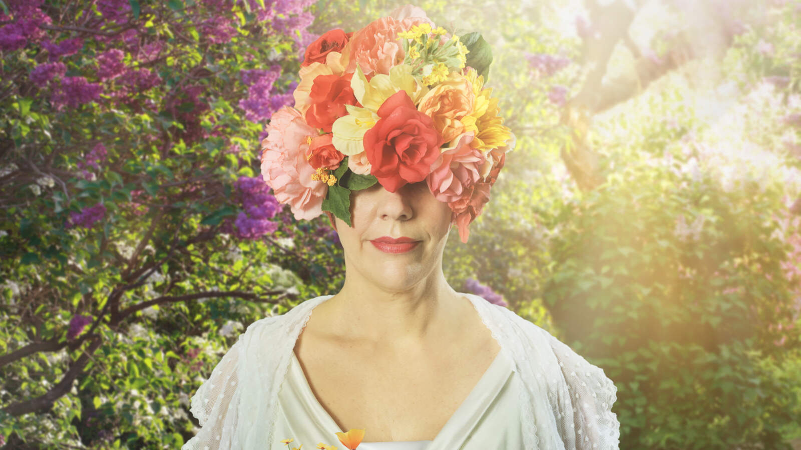 En person som bär en huvudbonad täckt av färgglada blommor står bland blommor i en solig, frodig trädgård.