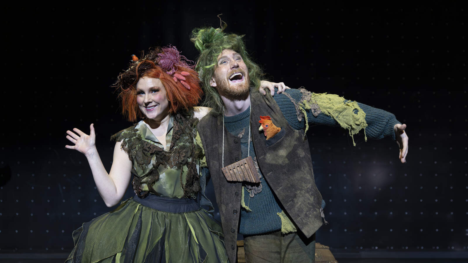 Papageno står med armen om Papagena, som vinkar. Båda ler.