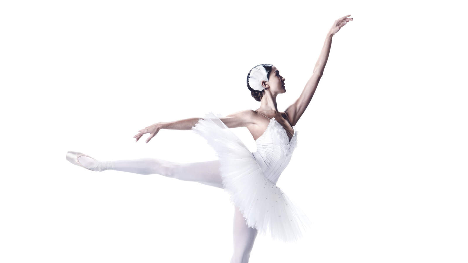 En ballerina i vit tutu balanserar på ena tån med en arm sträckt fram och ett ben utsträckt bakom sig.