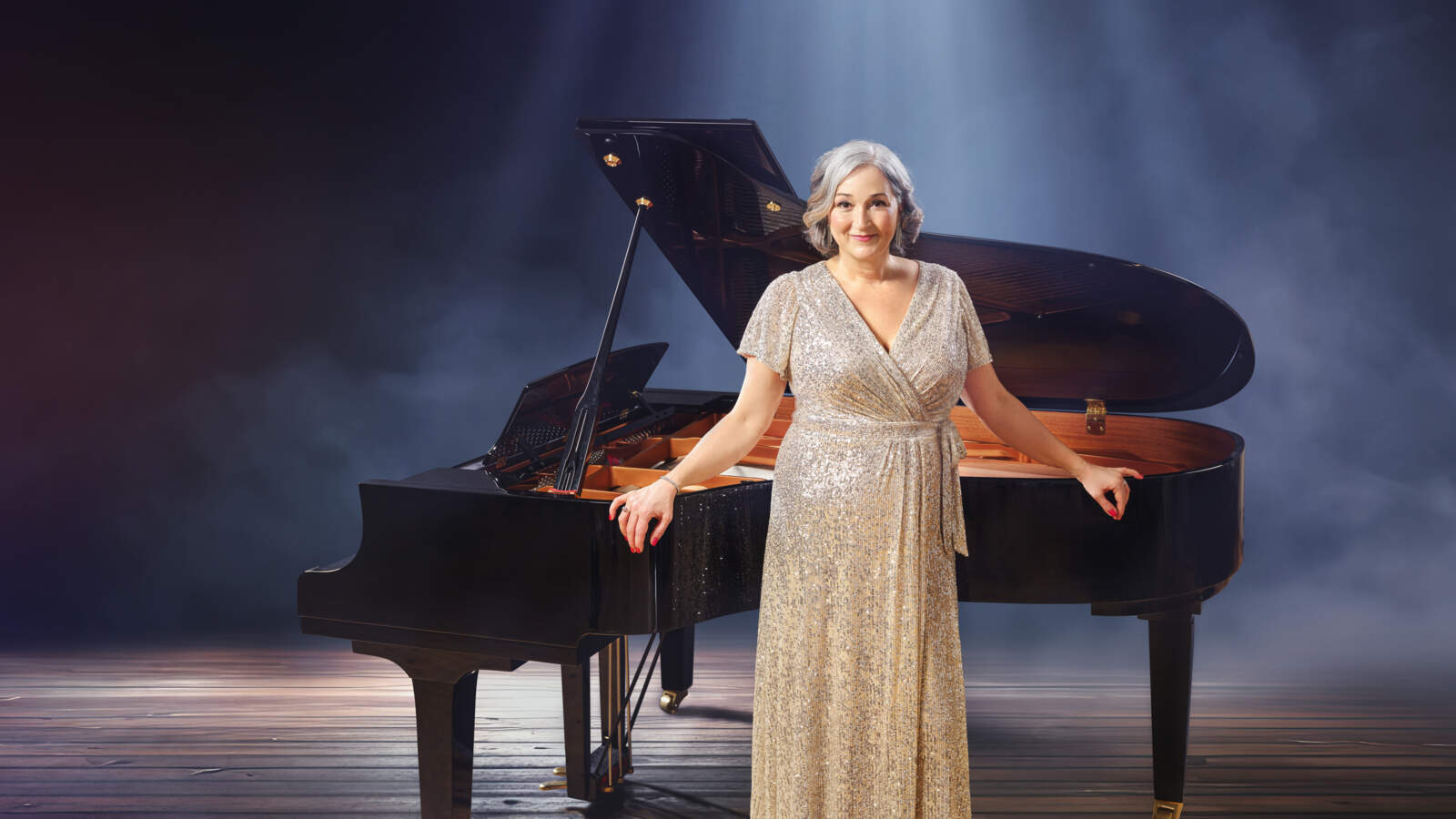 En operasolist i silverglittrig klänning står lutad mot en flygel på en annars tom scen under ljus.