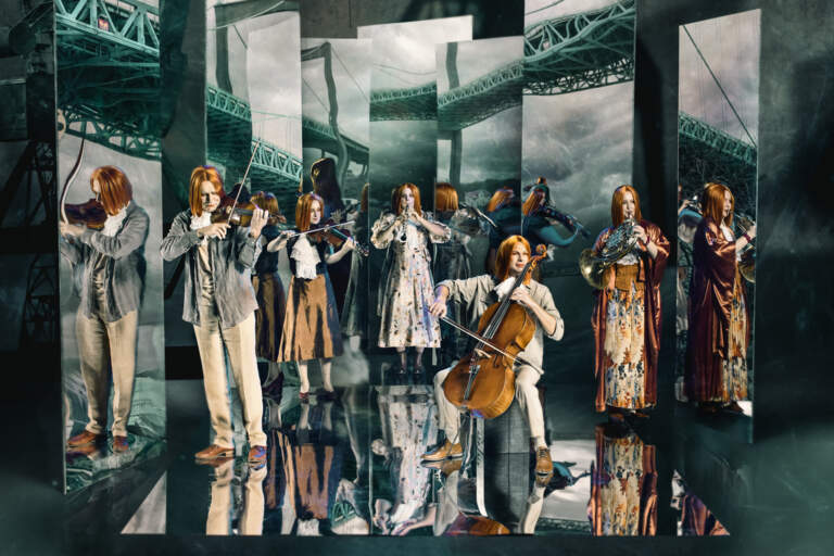 Sex orkestermedlemmar spelar sina instrument medan de står framför sju högsmala speglar. Älvsborgsbron syns i speglarna.